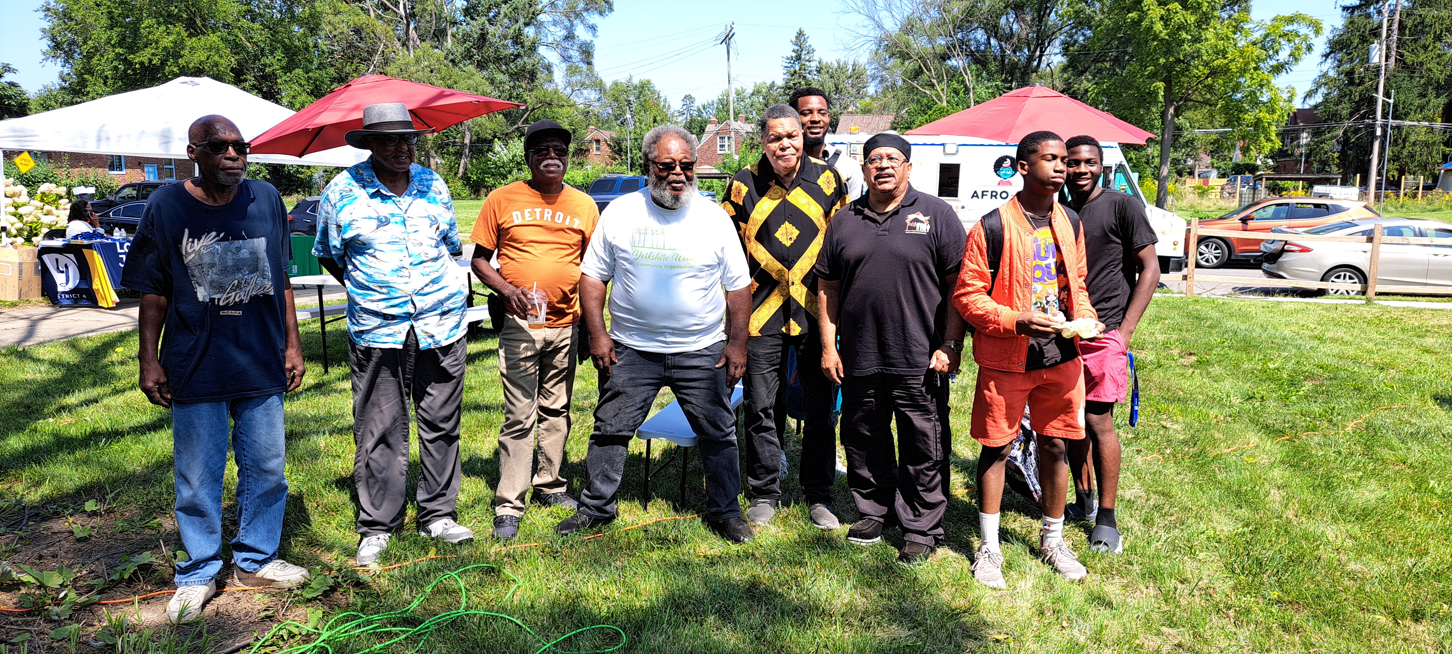 Nine community members smile at the camera in front of festival tents.