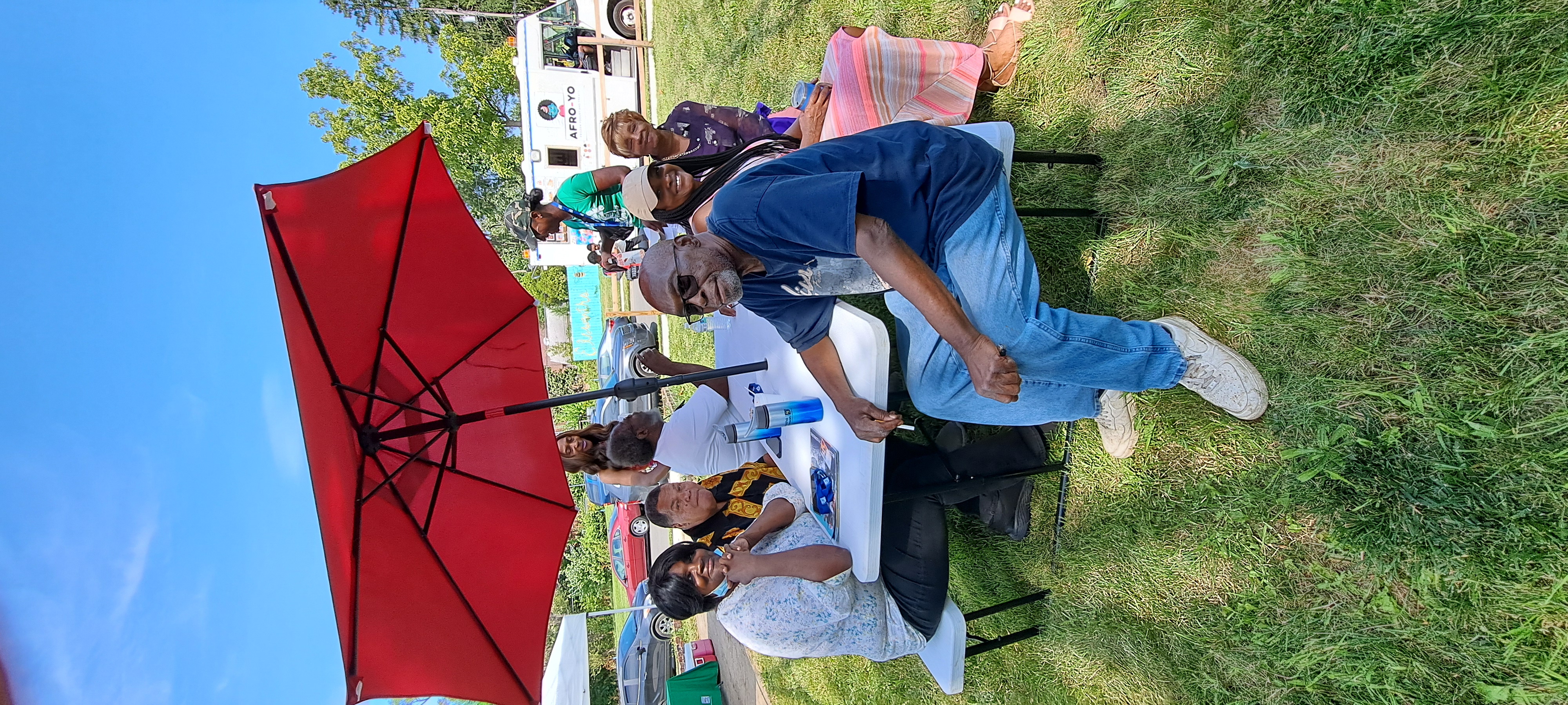 Smiling residents sit on a picnic bench beneath a sun umbrella.