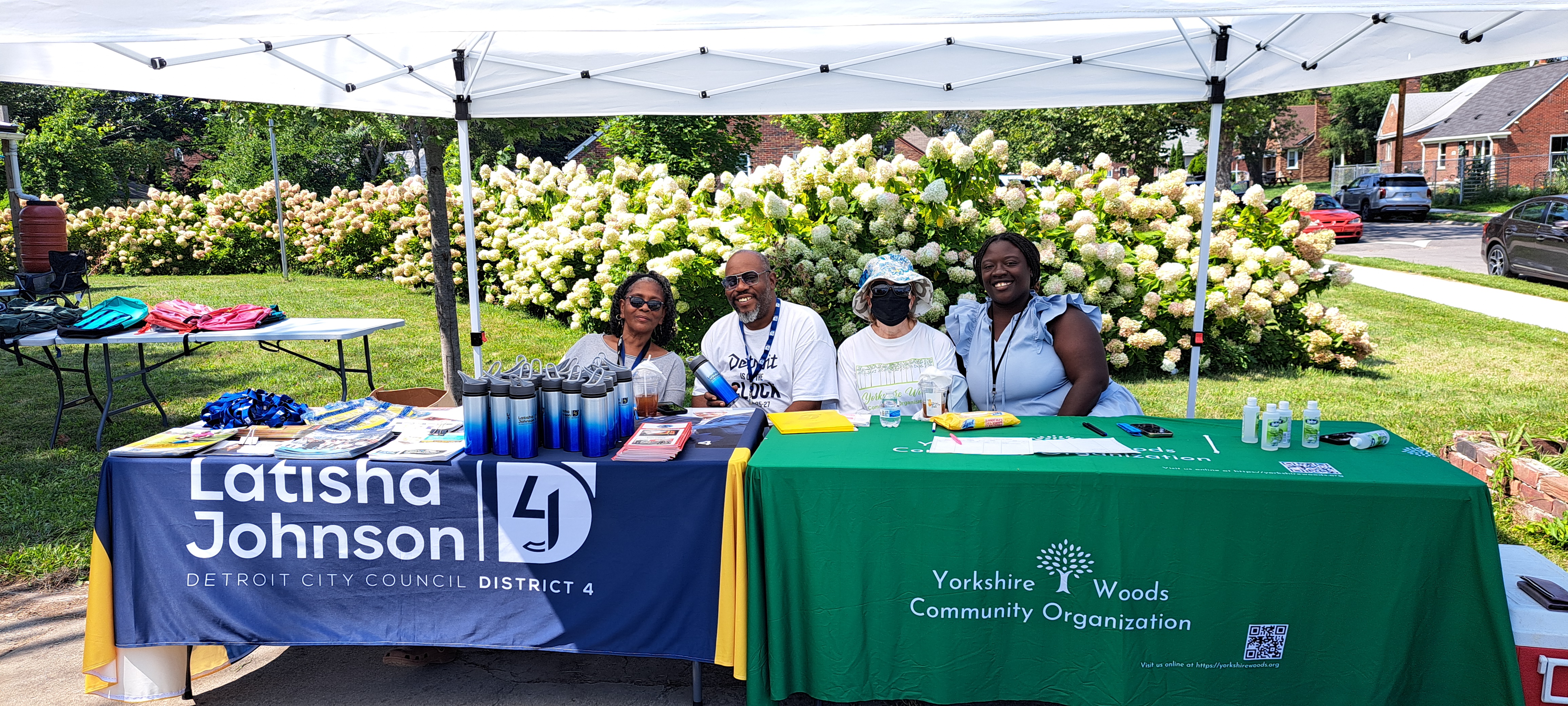 Representatives from Councilwoman Johnson's office post next to representatives from Yorkshire Woods Community Organiztion. Both groups sit at their respective tables, each decorated with custom tablecloths.
