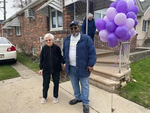 In front of a house decorated with a bunch of purple balloons, Ms. Lottie poses with Yorkshire Woods Community Organization president Mose Primus.